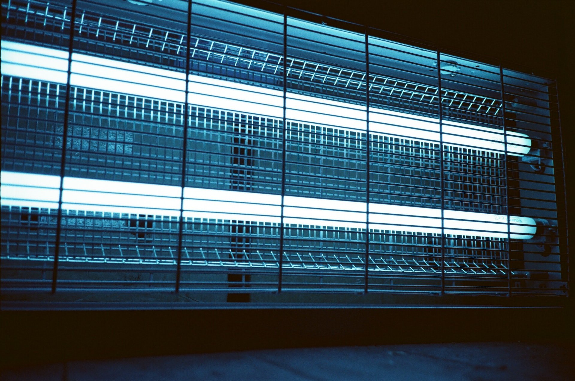 A bug zapper equipped with commercial lighting features two glowing blue fluorescent lights behind a protective metal grid, promising both efficiency and durability.