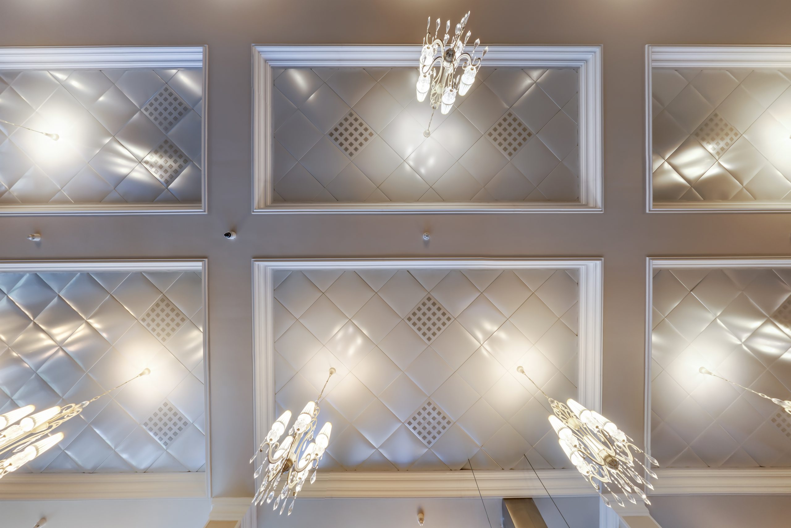 Halogen Lamps Elegant ceiling with quilted panels and ornate chandeliers, viewed from below.