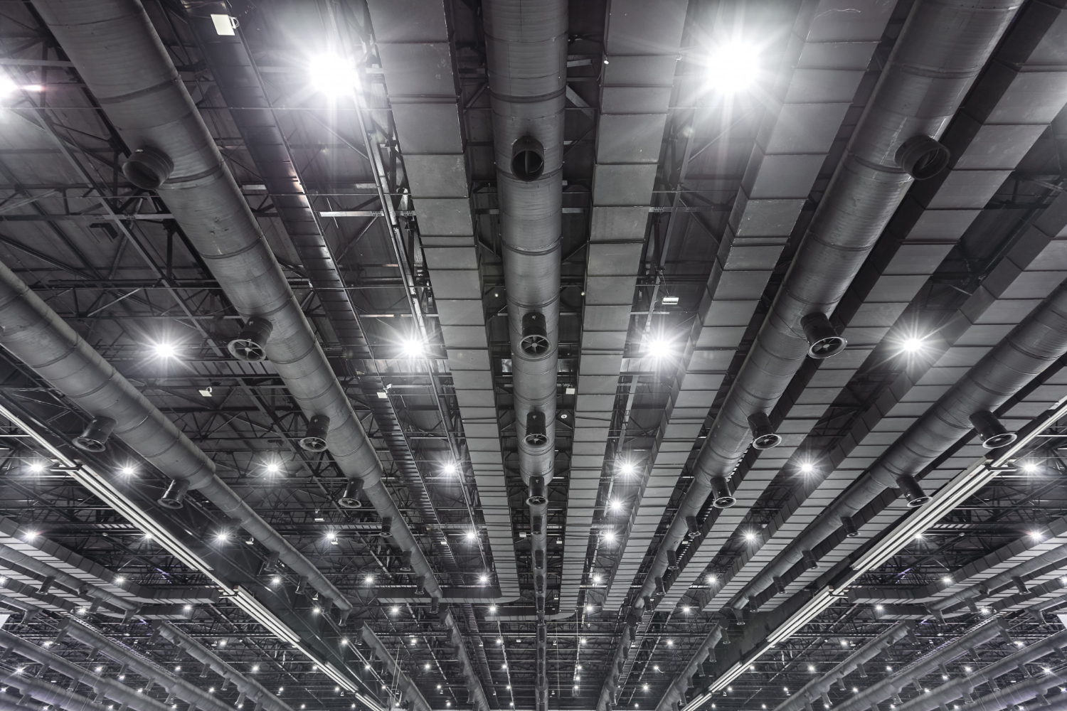 Dark industrial ceiling with exposed pipes and bright overhead lights.