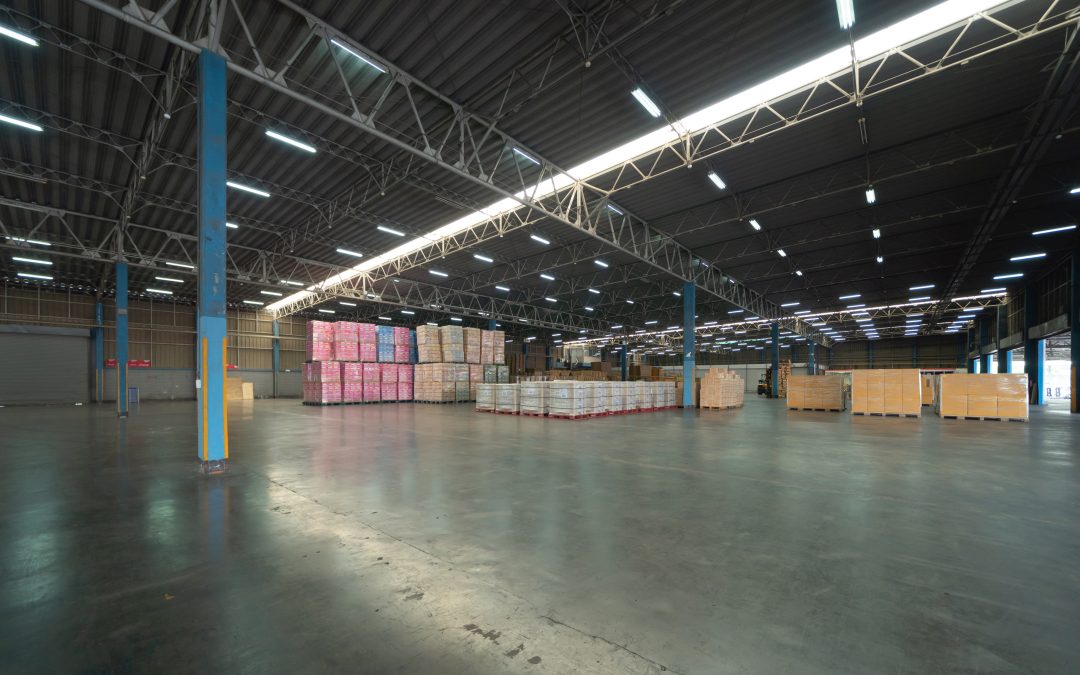 Spacious warehouse interior with stacked pallets and boxes under bright overhead lighting.