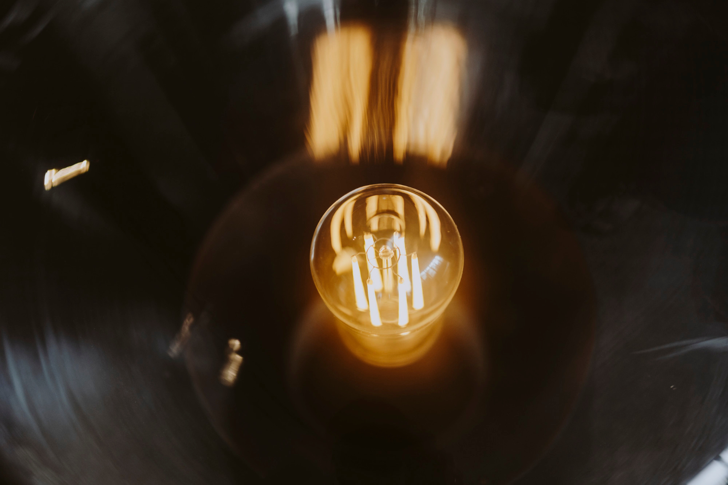 Close-up of a glowing light bulb, viewed from above, with warm lighting temperature reflections on a dark background.